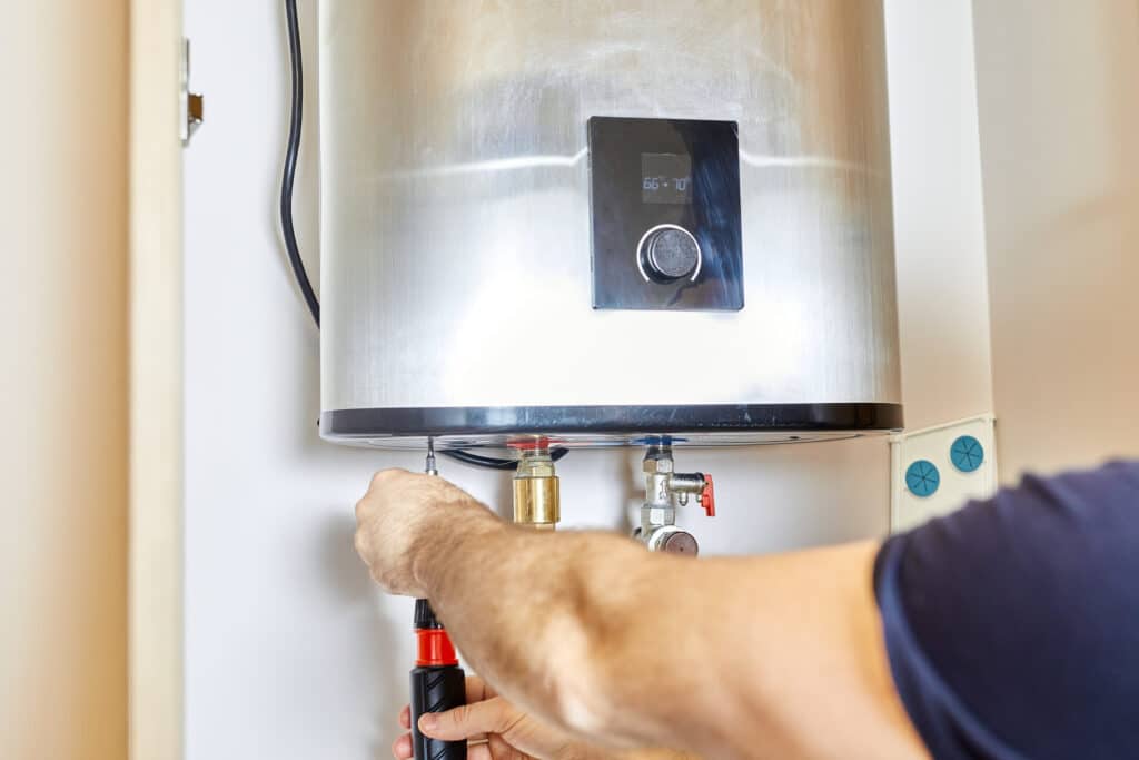A person adjusts a hose attached to a stainless steel, tankless water heater in a home.